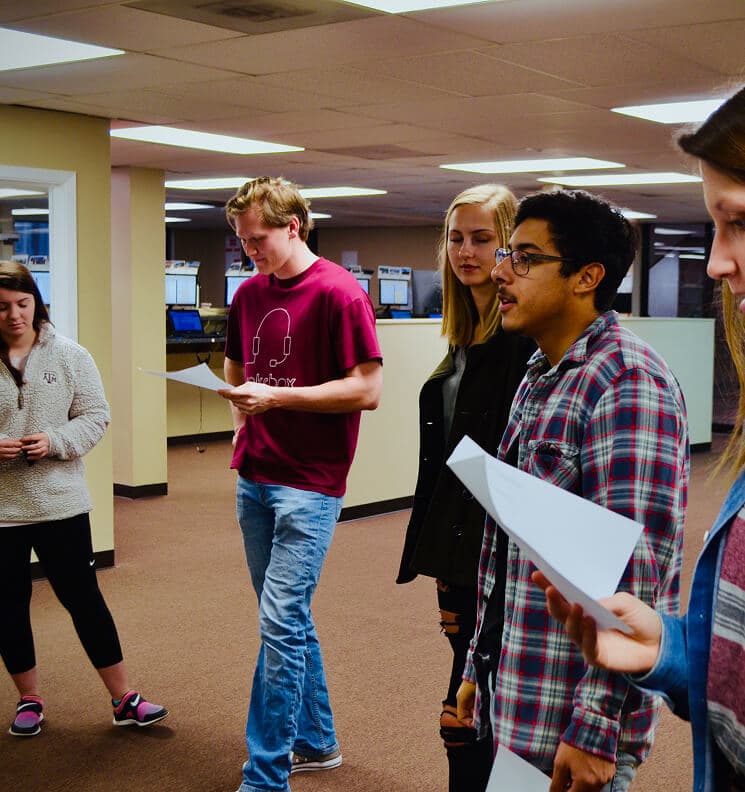 Five rokrbox callers stand in the call floor holding printed scripts during a group roleplay session